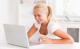 Cute woman having a cup of tea while using her notebook